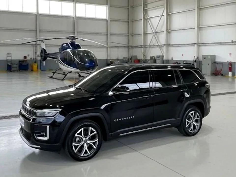 SUV executivo Jeep Commander preto em hangar de aviação executiva, com helicóptero ao fundo