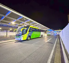 Ônibus rodoviário à noite junto à cobertura iluminada de um terminal de embarque